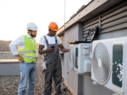 Repairmen with multimeter fixing air conditioner on rooftop